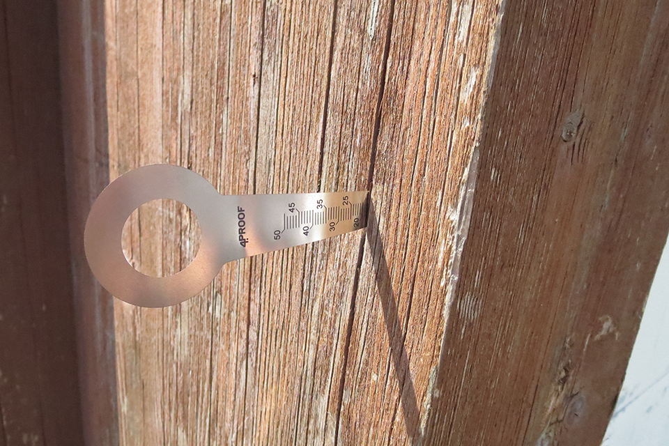 Eine metallene Risstiefenlehre steckt in einem alten Holzbalken.