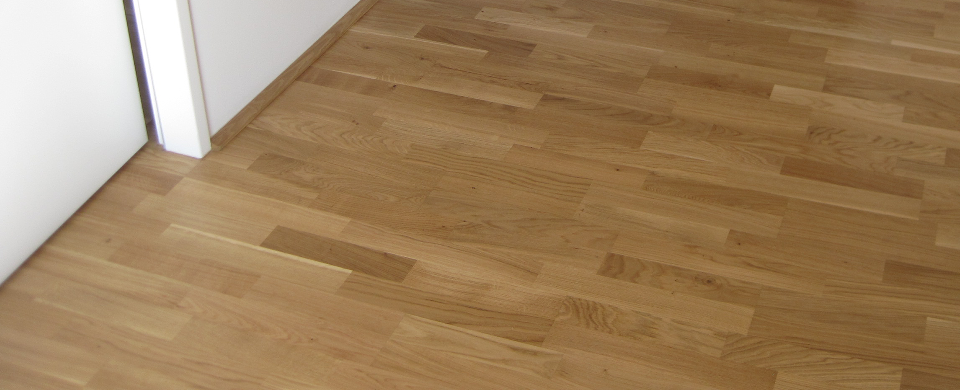 Holzfußboden, der an eine weiße Wand grenzt.