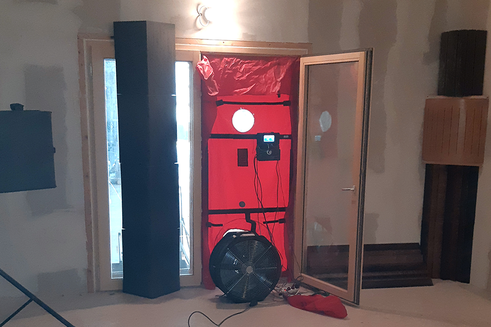 Eine rote Blower-Door-Messeinrichtung ist an einem Türelement angebracht.