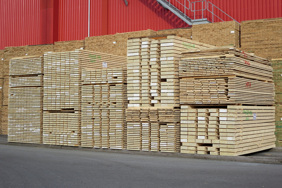 Schnittholzstapel im Werk vor einer roten Fassade.