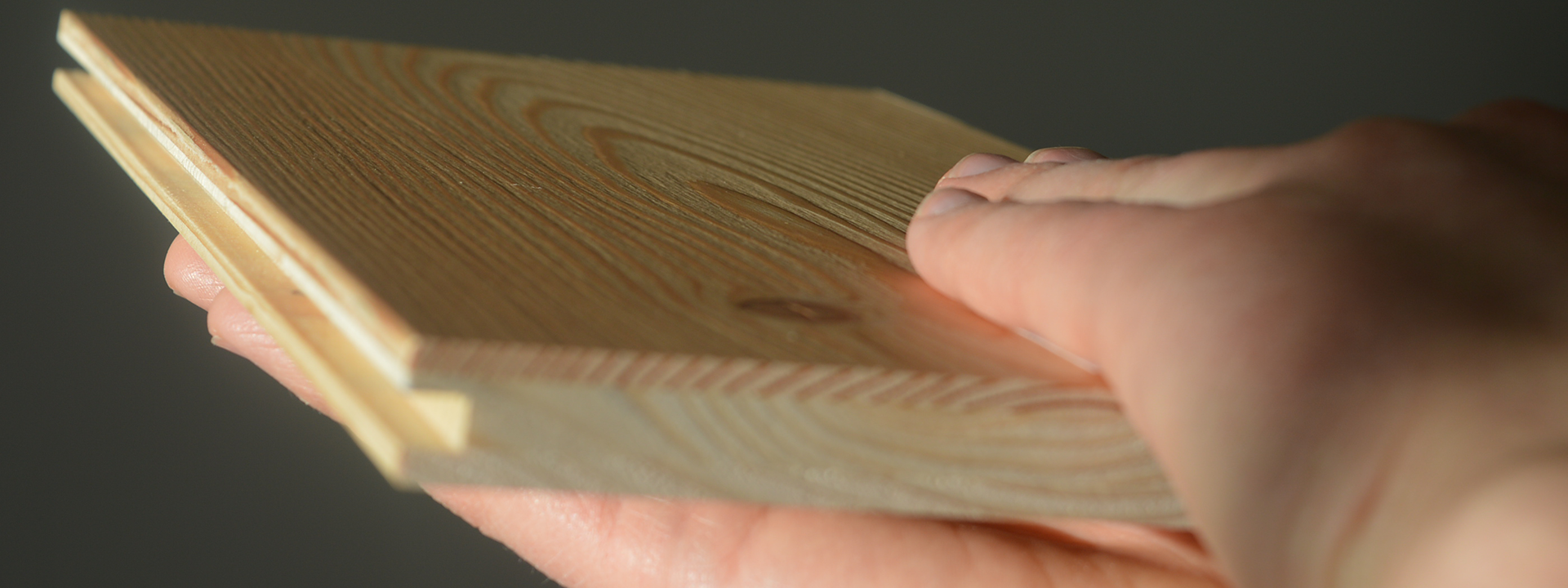 A hand strokes over a wooden plank to feel the surface texture.